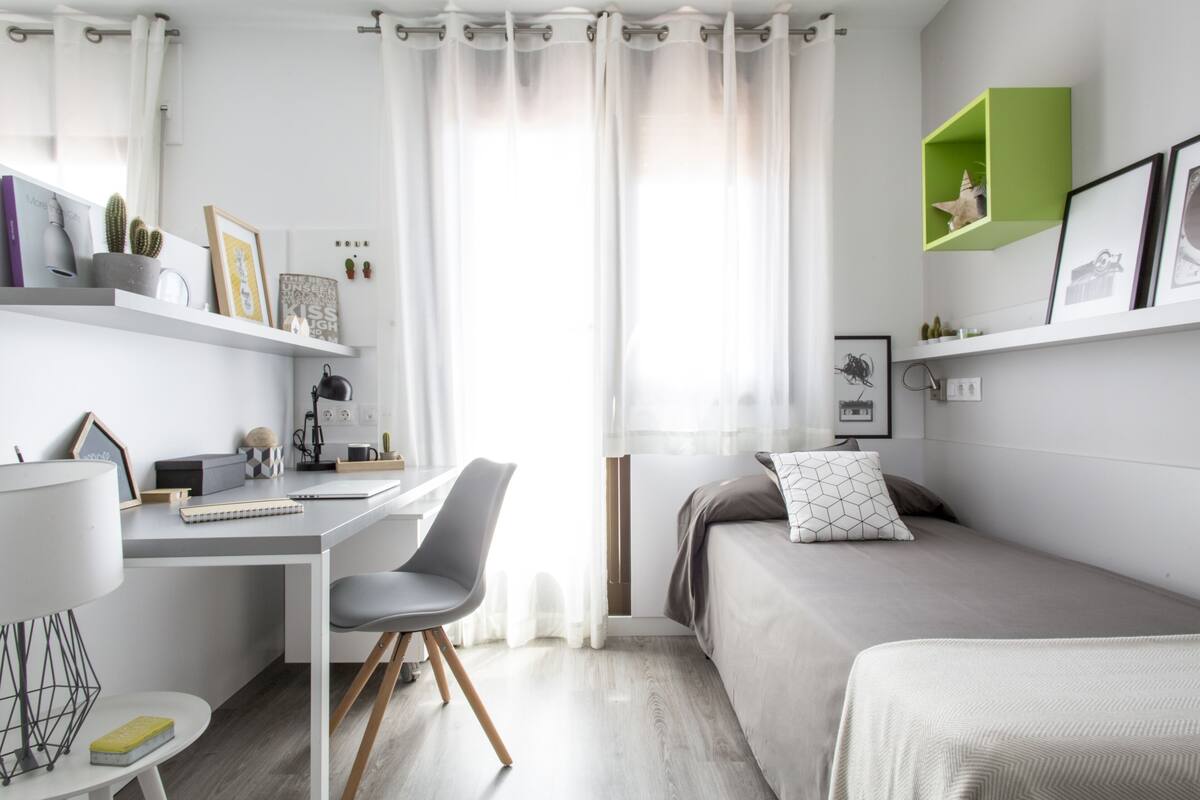 A modern bedroom with a desk, a bed, and a green shelf.