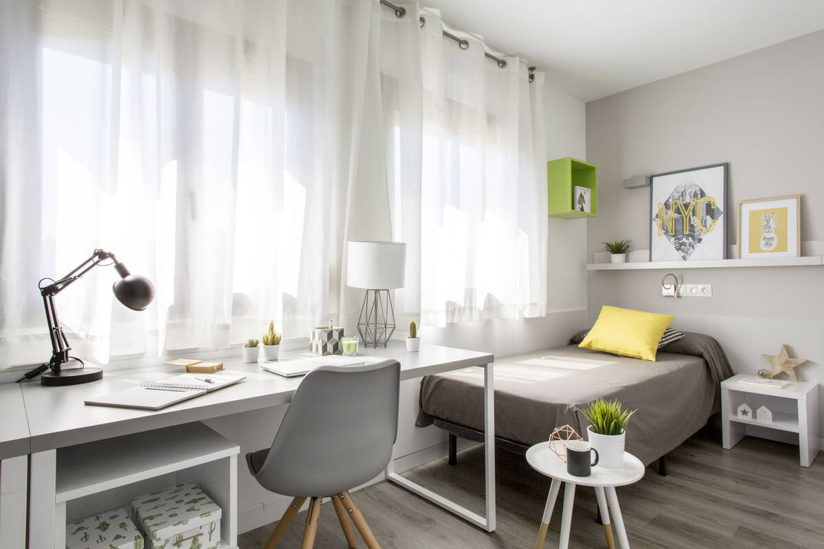 A modern bedroom with a desk, chair, bed, and bedside table.