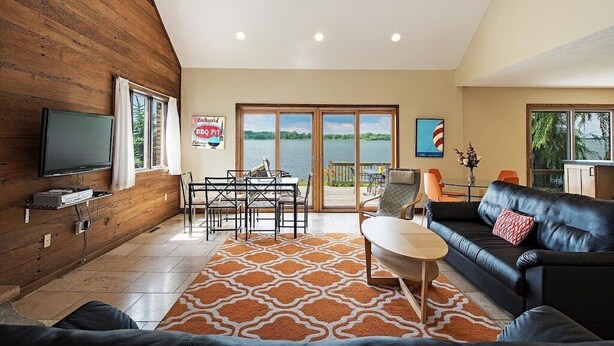 A modern living room with a TV, dining table, and sofa, overlooking a scenic view.