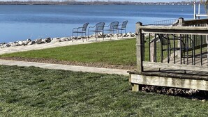 A lakeside park with a wooden deck, metal chairs, and a stone pathway.