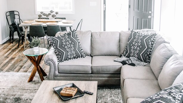 A living room with a sectional sofa, a coffee table, a dining area with a table and chairs, a ceiling fan, and a wall-mounted sign that reads "LAKE".