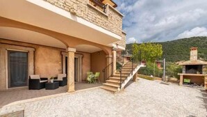 A stone building with a covered patio, outdoor seating, and a staircase leading to a second floor. - L'Arcobaleno Di Chia (Domus de Maria)