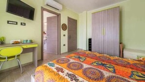 A bedroom with a bed, a desk, a chair, a wardrobe, and a television on the wall. - L'Arcobaleno Di Chia (Domus de Maria)
