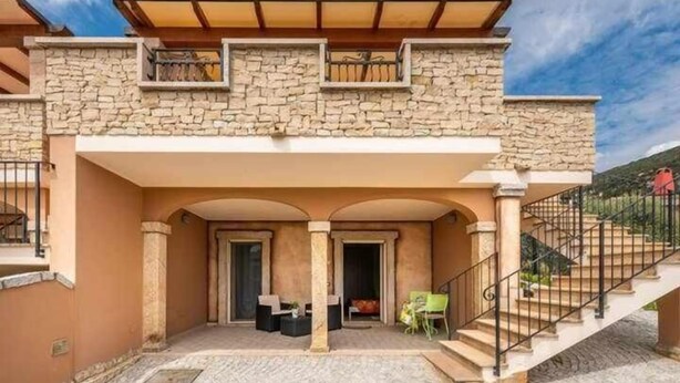 A two-story building with a stone facade, a covered patio area with outdoor seating, and a staircase leading to an upper level. - L'Arcobaleno Di Chia (Domus de Maria)