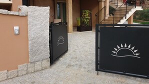 A gated entrance with a stone wall and a metal gate featuring a sun design. - L'Arcobaleno Di Chia (Domus de Maria)