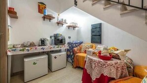 A compact living space with a kitchenette, a bed with a patterned bedspread, and a staircase leading to an upper level. - L'Arcobaleno Di Chia (Domus de Maria)