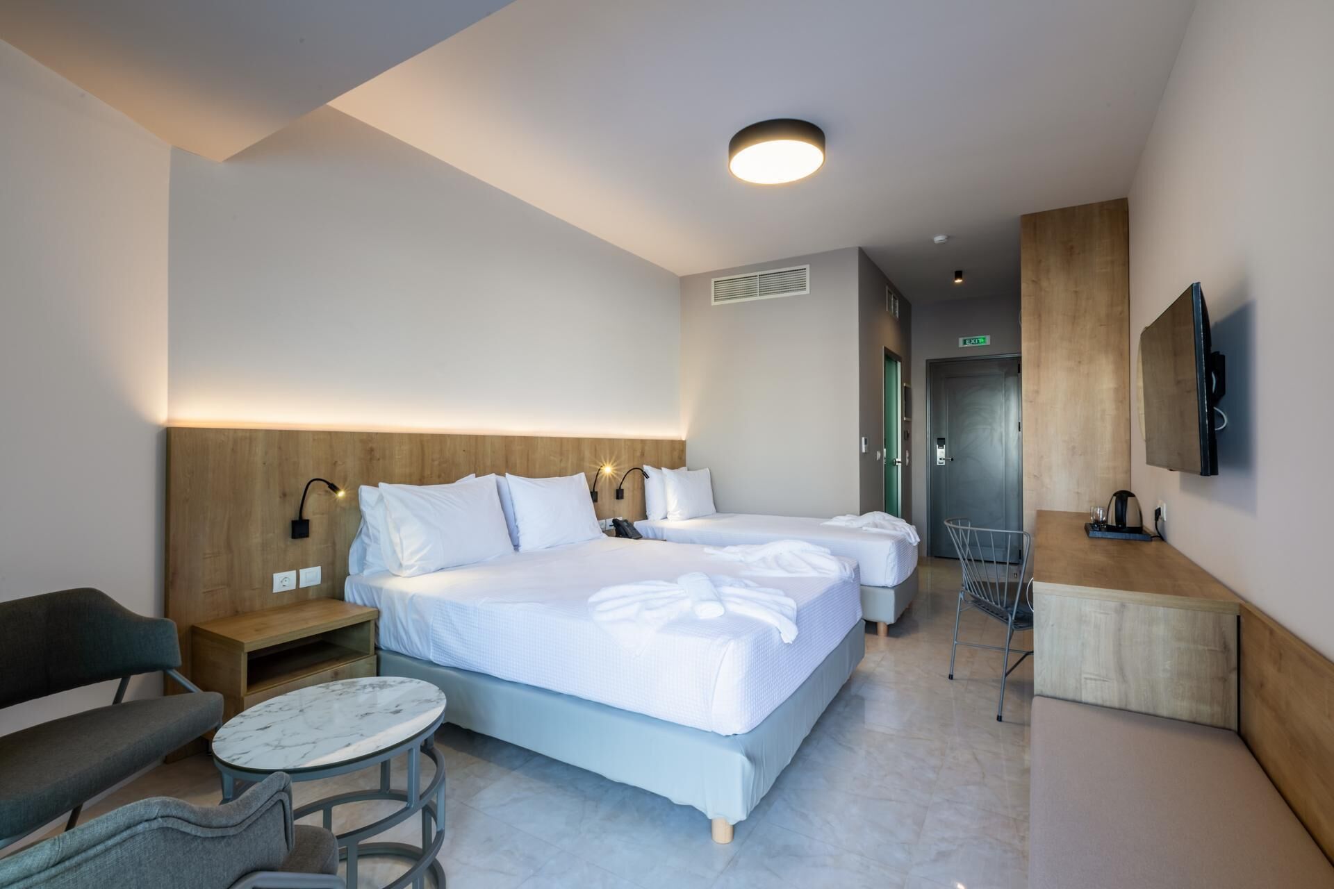 A hotel room with two beds, a desk, a chair, a small table, and a TV mounted on the wall.