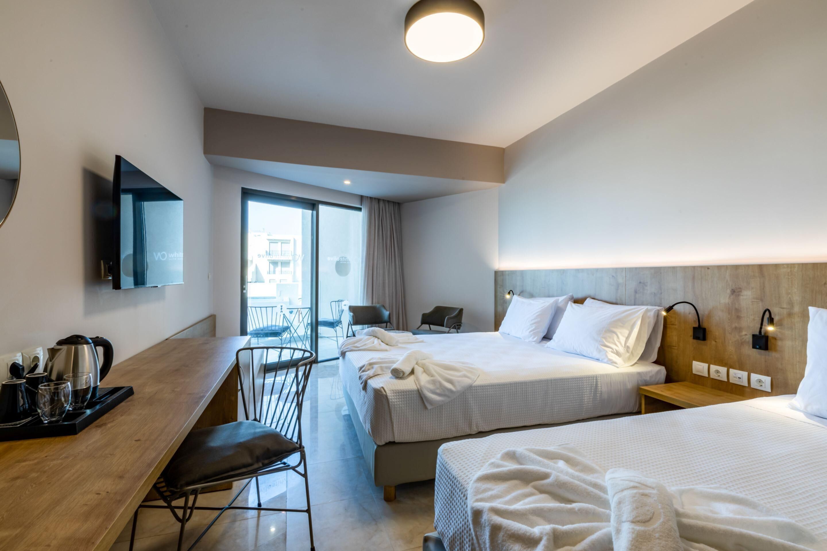 A hotel room with two beds, a desk with a chair, a TV, and a balcony with a view.