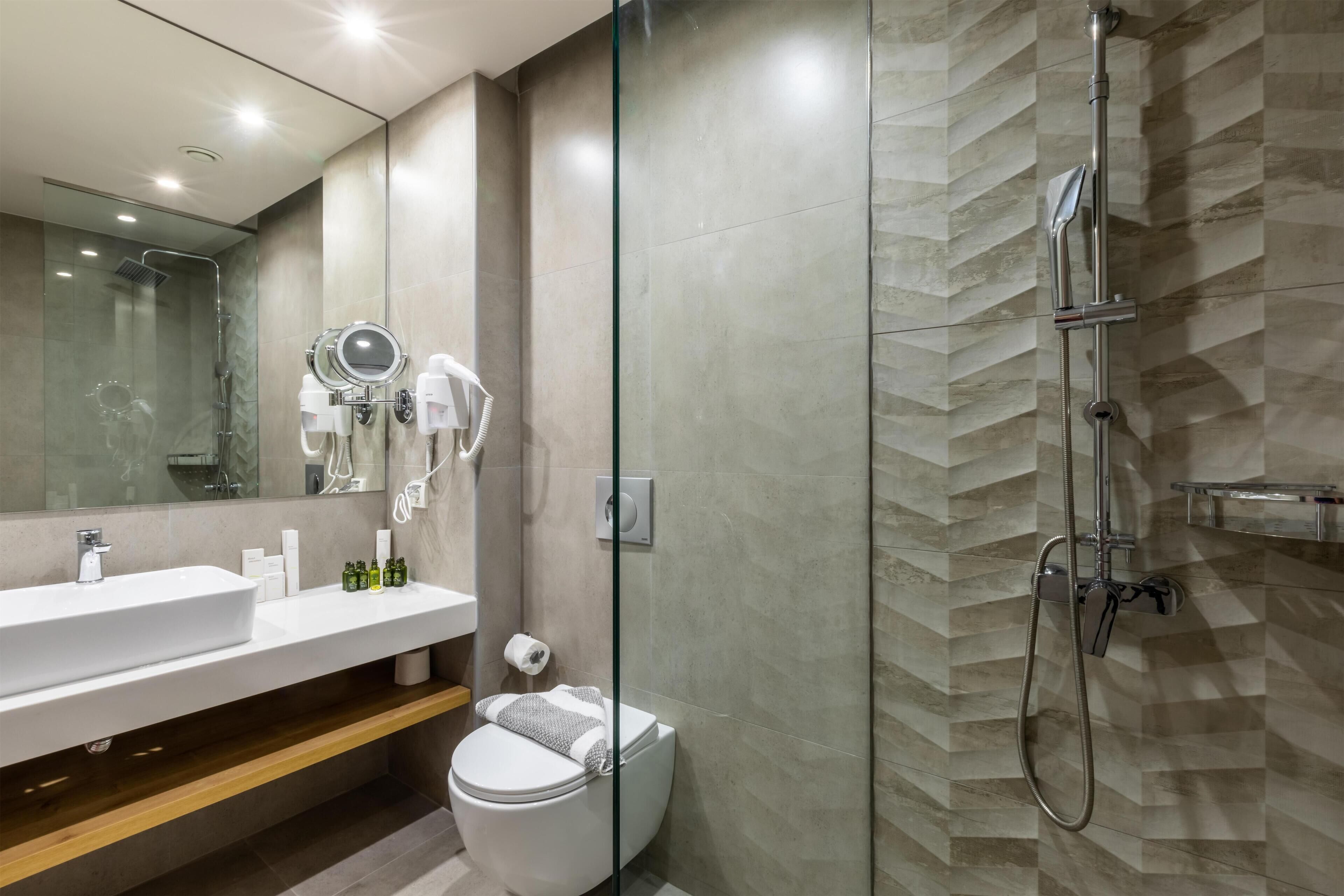 Un baño moderno con ducha envuelta en vidrio, un espejo grande y un tocador con lavabo y toallero.