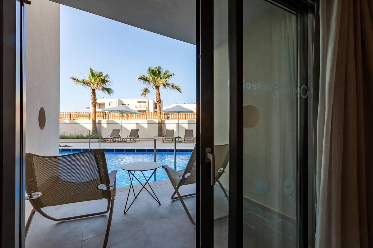 A balcony with a pool, two palm trees, and lounge chairs.