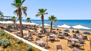 A beachside resort with outdoor seating and palm trees. - White Olive Elite Rethymno - All Inclusive (Rethymno)
