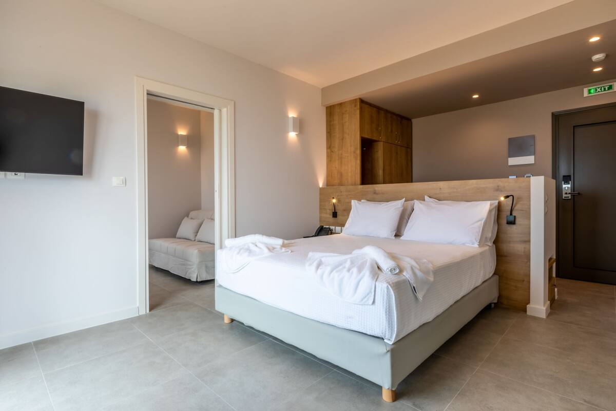 A modern hotel room with a large bed, a TV mounted on the wall, and a wooden headboard.