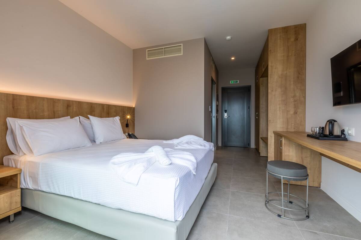 A modern hotel room with a large bed, a wooden headboard, a small desk, and a mirror.