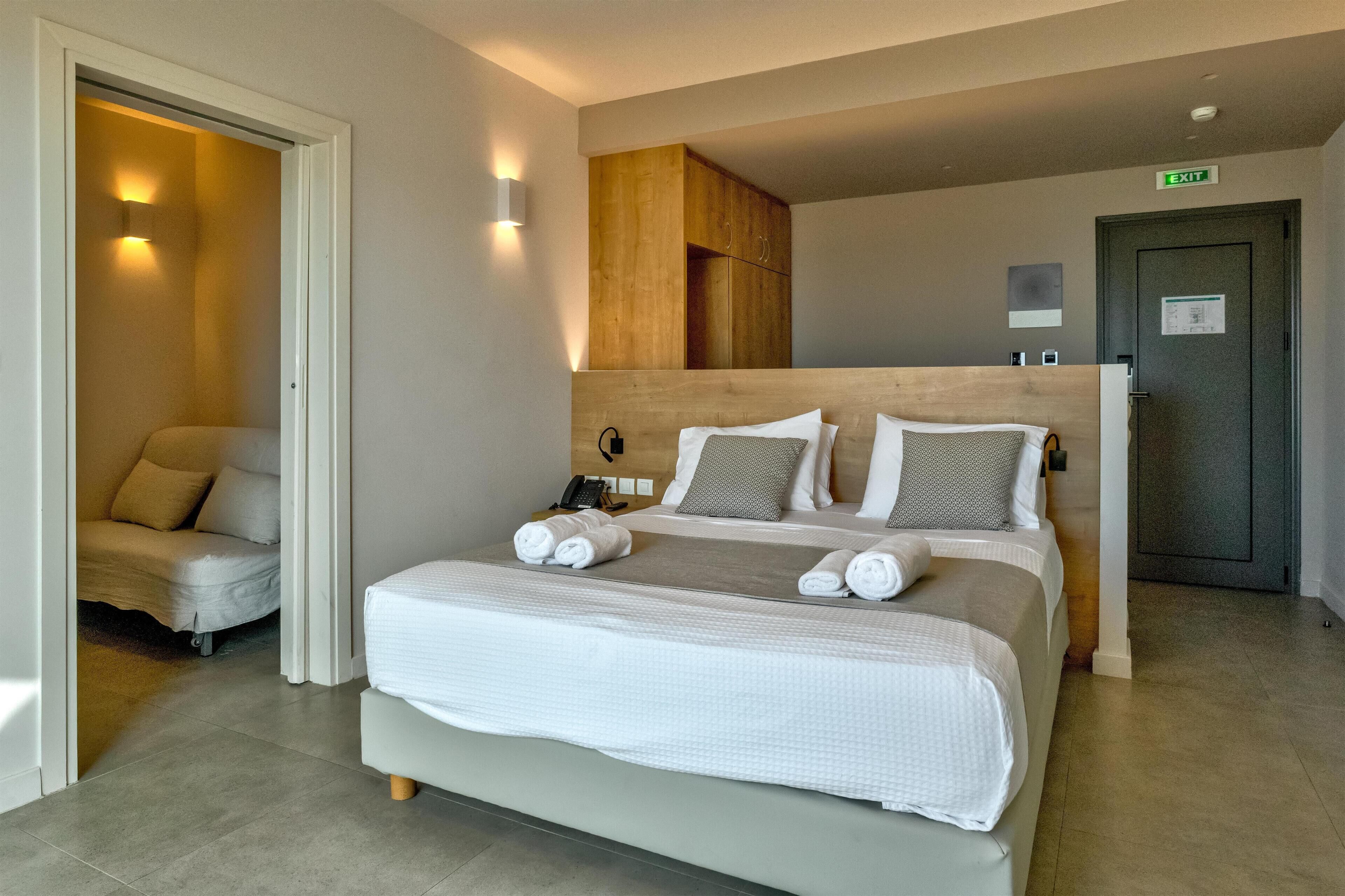 Een moderne hotelkamer met een groot bed, een houten hoofdbord en een zithoek met een bank.
