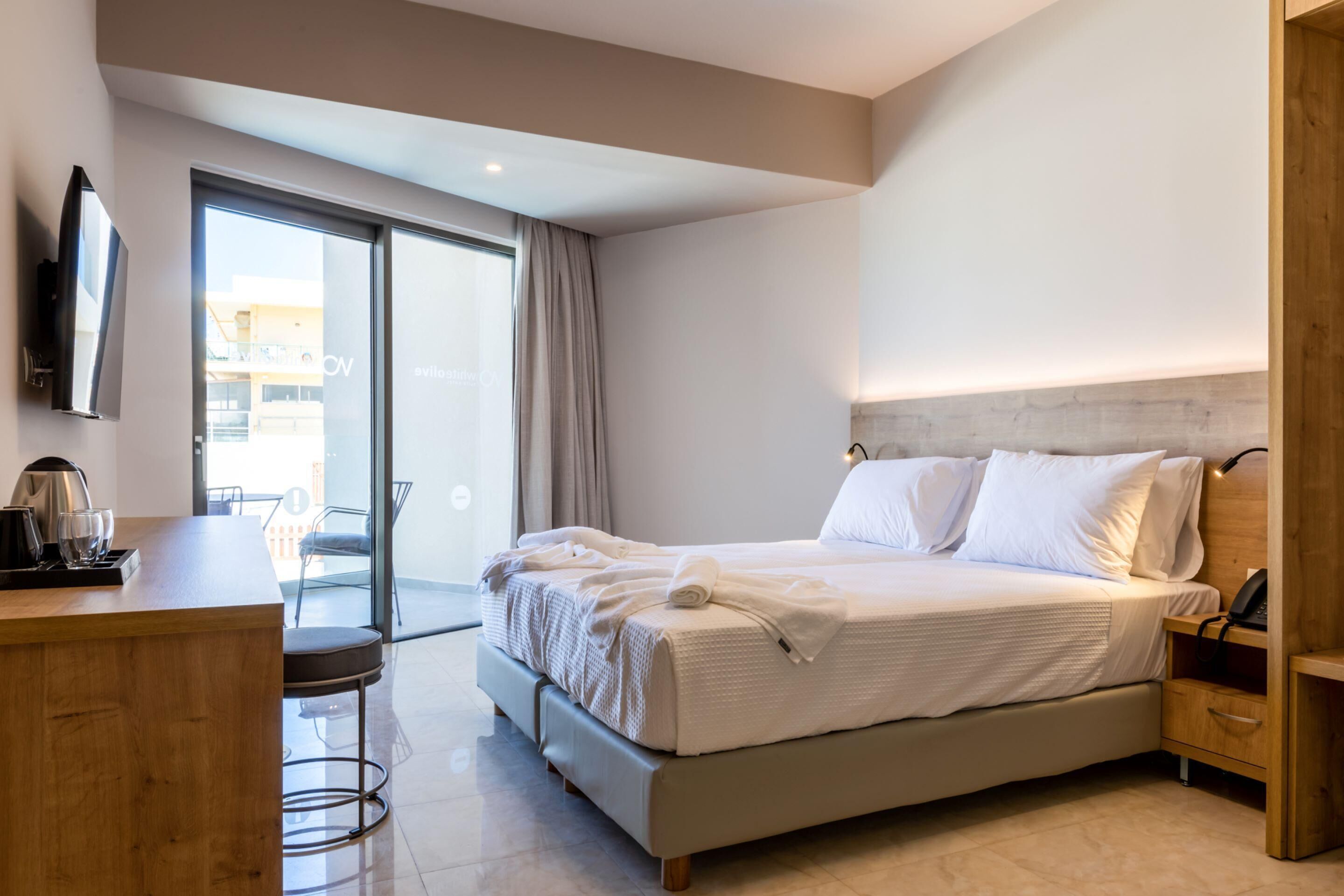 A modern hotel room with a large bed, a desk with a kettle, and a TV mounted on the wall.