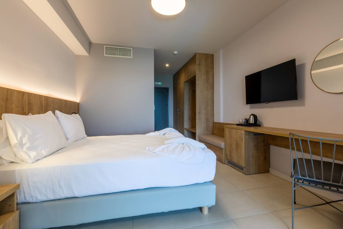 A modern hotel room with a large bed, a desk, a chair, a TV, and a mirror.