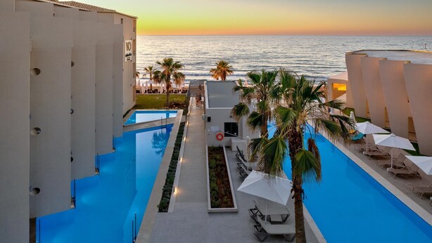 A pool area with a view of the sea, palm trees, and lounge chairs. - White Olive Elite Rethymno - All Inclusive (Rethymno)