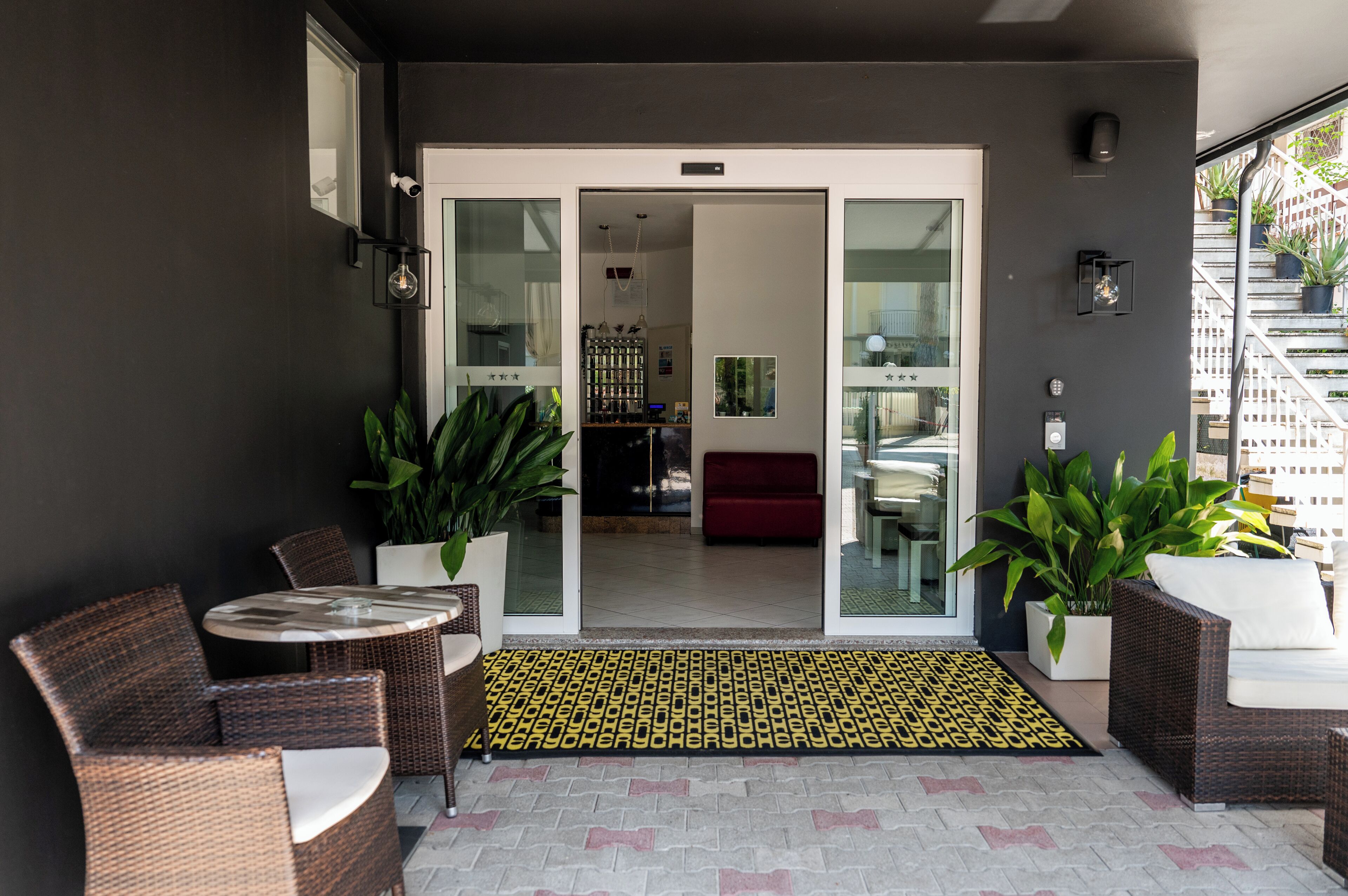 A modern outdoor seating area with wicker furniture, a glass door entrance, and potted plants.
