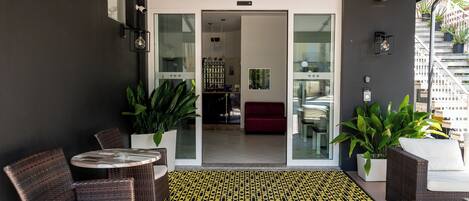 A modern outdoor seating area with wicker furniture, a glass door entrance, and potted plants.