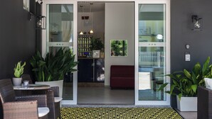 Un interior moderno con puerta de vidrio, muebles de mimbre, plantas en macetas y un suelo estampado.