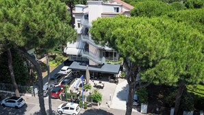 Un hotel con terraza en la azotea, una escalera que lleva al piso superior y un estacionamiento con varios autos.