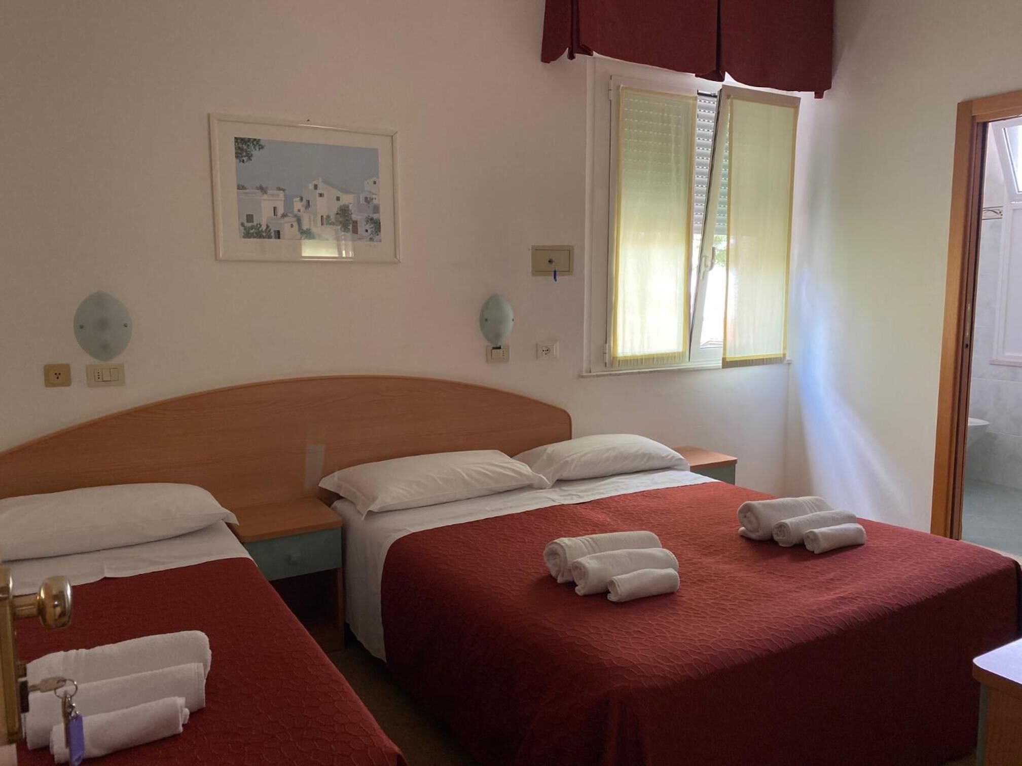 A hotel room with two beds, a painting on the wall, and a window with blinds.