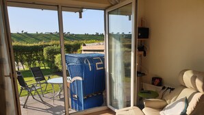 A room with a sliding glass door leading to a patio with a table and chairs, a blue woven chair, and a beige sofa with a footrest.