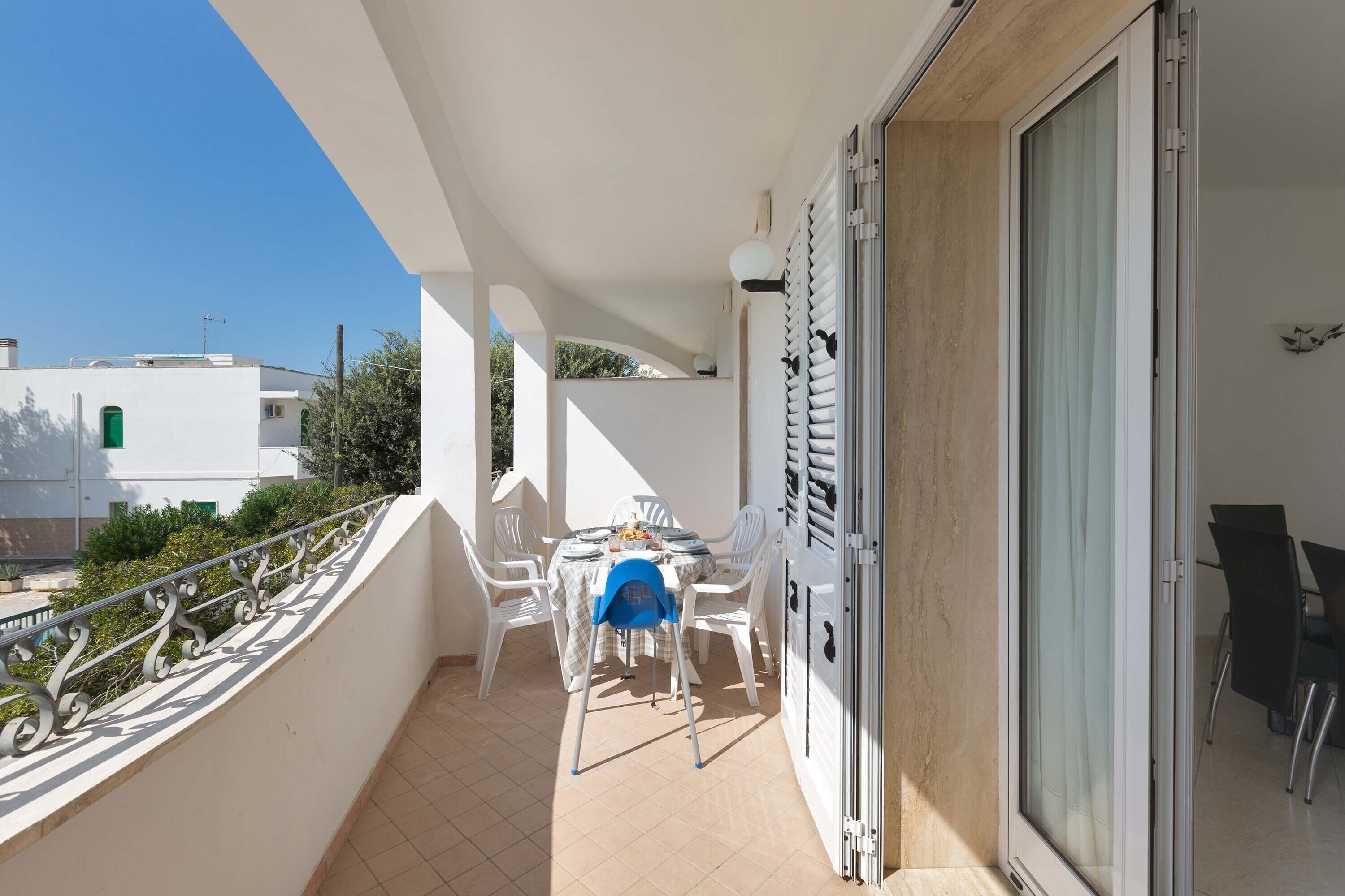 A balcony with a table and chairs, a sliding glass door, and a view of neighboring buildings.