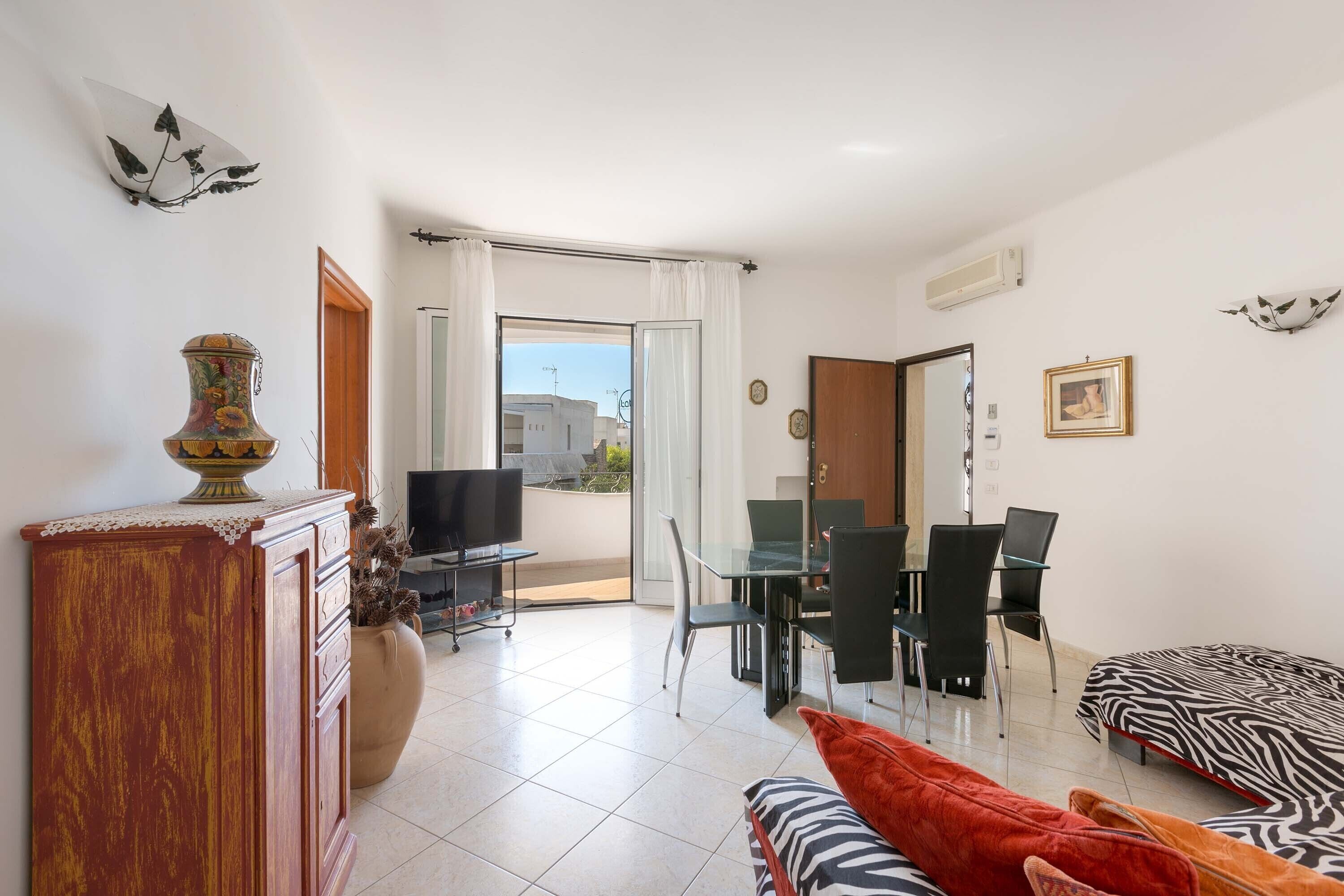 A modern living room with a dining area, a TV, and a balcony with a view.