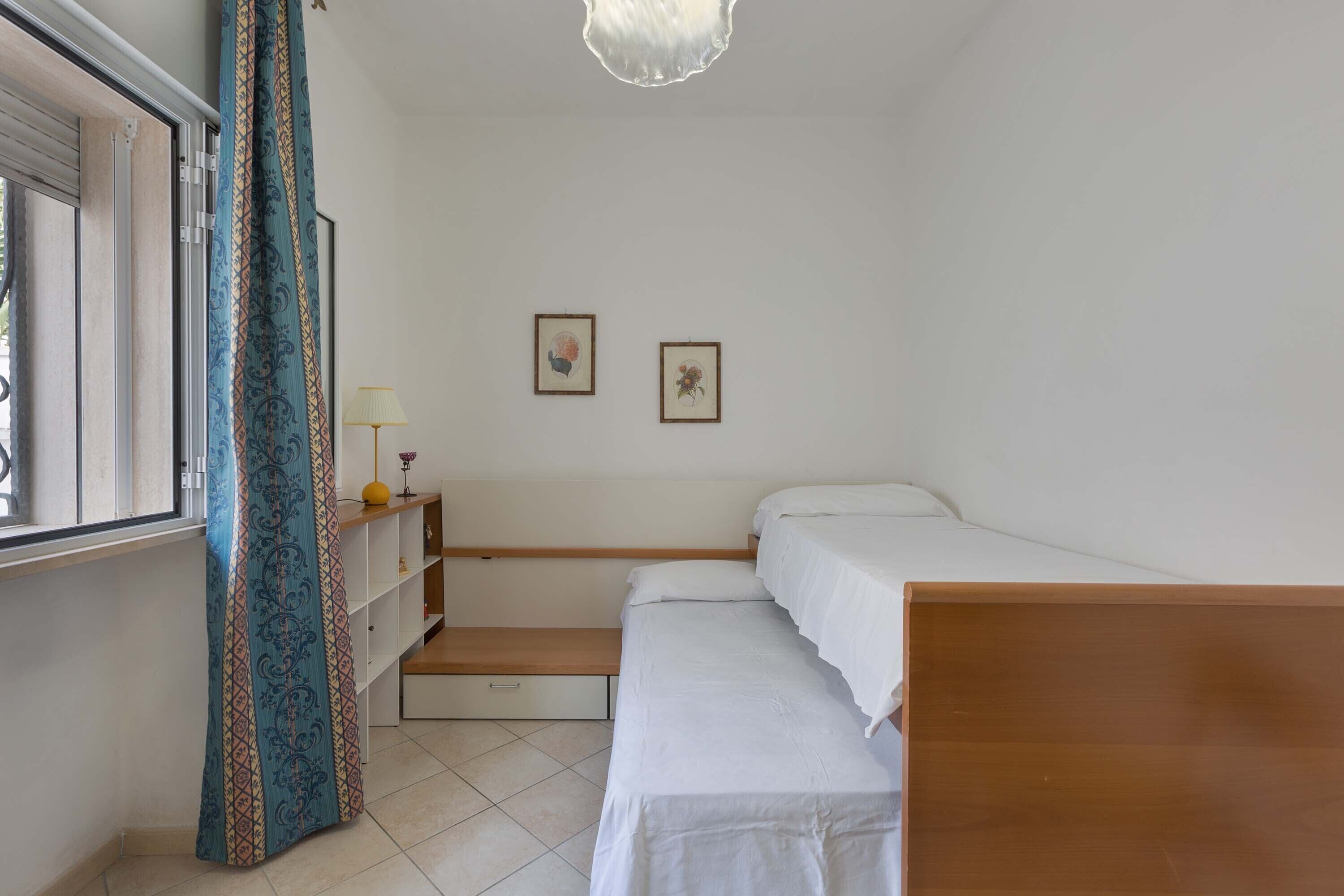 A bedroom with a bed, a bedside table with a lamp, and two framed pictures on the wall.