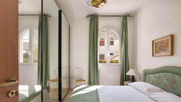 Quarto com cama, cadeira, luminária e janela com cortinas.