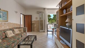 Uma sala de estar com sofá, mesa de centro, televisão e um espaço de jantar com cadeiras e mesa.