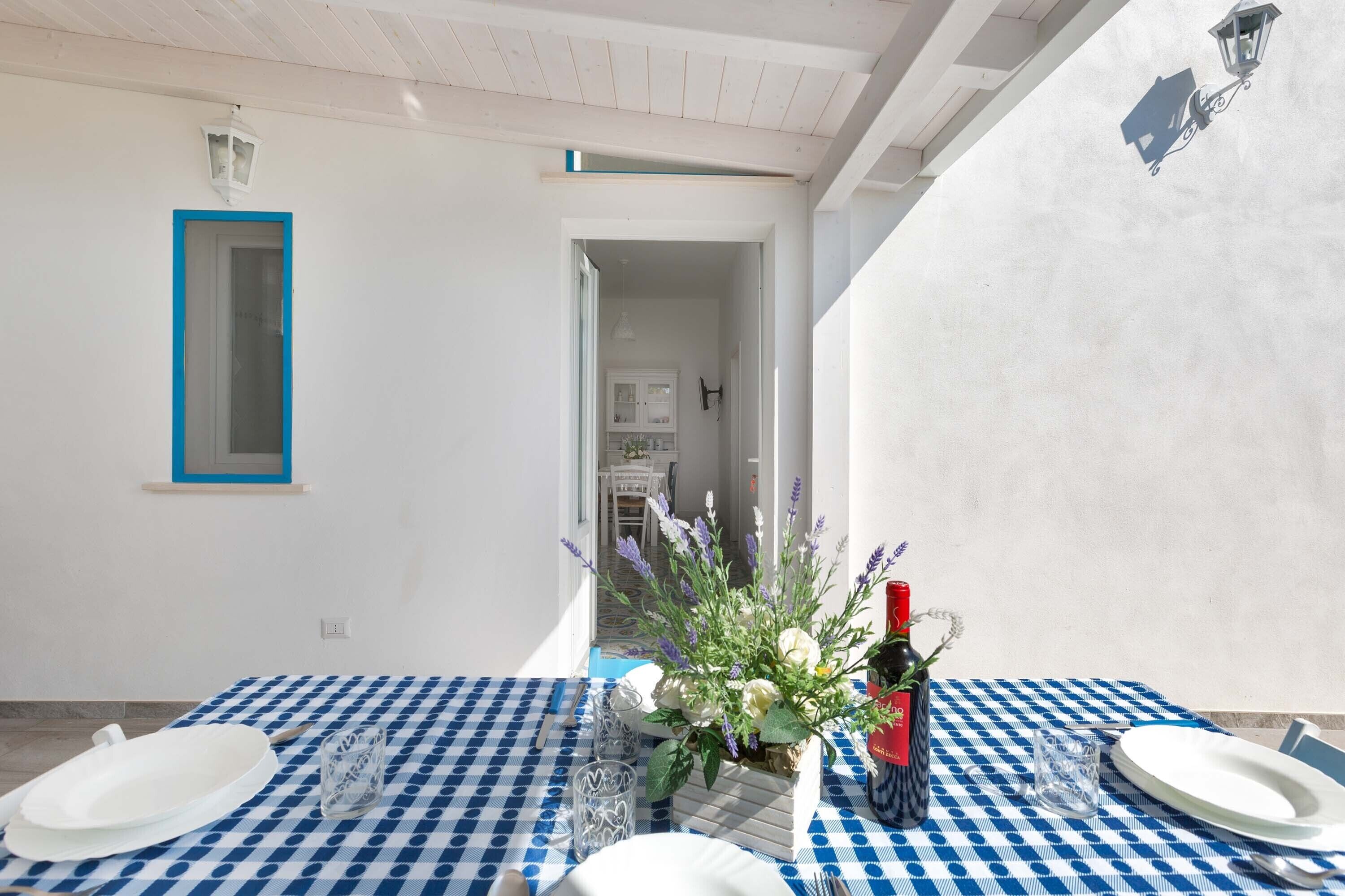 A dining area with a checkered tablecloth, a white table, and a vase of flowers.