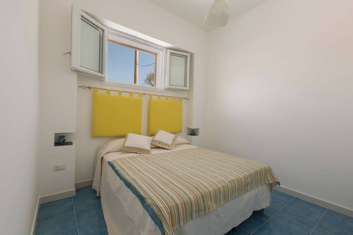 Un dormitorio con cama, ventana y mesita de noche.