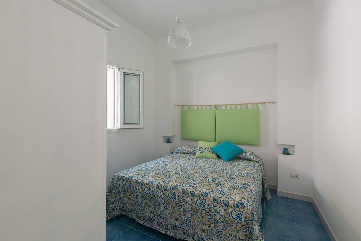 Un dormitorio con una cama, un cabecero verde, una ventana y una lámpara colgante.