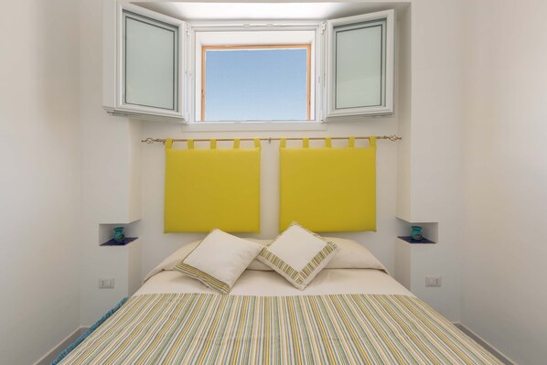 Une chambre à coucher avec un lit, deux têtes de lit jaunes, une fenêtre au-dessus du lit et une couvre-lit à rayures.