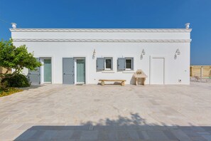 A white building with a stone-paved courtyard, a bench, and a small table. - 1695 Villa Albarosa by Perle di Puglia (Ruffano)
