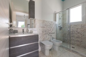 A modern bathroom with a marble shower, a glass-enclosed shower, a toilet, and a vanity with a mirror. - 1695 Villa Albarosa by Perle di Puglia (Ruffano)