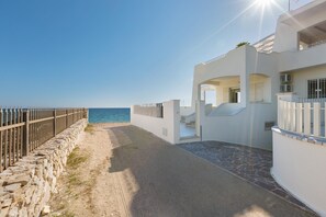 A coastal building with a stone pathway leading to a beach, a metal fence, and a clear view of the sea. - Villa Diamante (Maruggio)