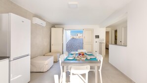 Une cuisine moderne avec des appareils électroménagers blancs, une table à manger dressée pour quatre personnes et une vue sur un mur de pierre et un bâtiment à l’extérieur.