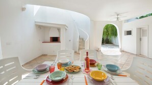 A dining area with a white table set for four, surrounded by white chairs. A spiral staircase is visible in the background, leading to an upper level. - Villa Oasi Marina (Maruggio)