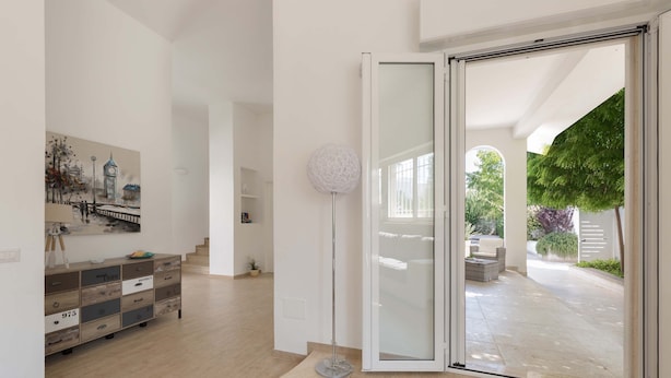 A spacious interior with a modern staircase, a large painting of a cityscape, and a glass door leading to an outdoor area with a patio and greenery. - Villa Oasi Marina (Maruggio)