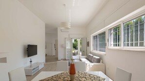 A modern living room with a flat-screen TV, a dining table with a vase, and a sofa with cushions. - Villa Oasi Marina (Maruggio)
