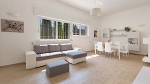 A modern living room with a sectional sofa, a dining table with chairs, and a large window providing natural light. - Villa Oasi Marina (Maruggio)