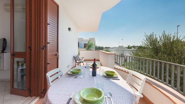 Un balcón con una mesa dispuesta para dos personas, una botella de vino y una silla.