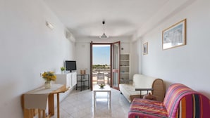 Una sala de estar con sofá, televisor, mesa de comedor y vistas al exterior.