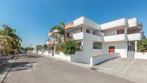 Un moderno edificio residencial de varios pisos con balcones, entrada con reja y vista despejada a la calle.