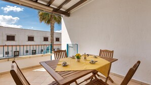 A covered patio with a table set for four, wooden chairs, a yellow tablecloth, and a small potted plant.