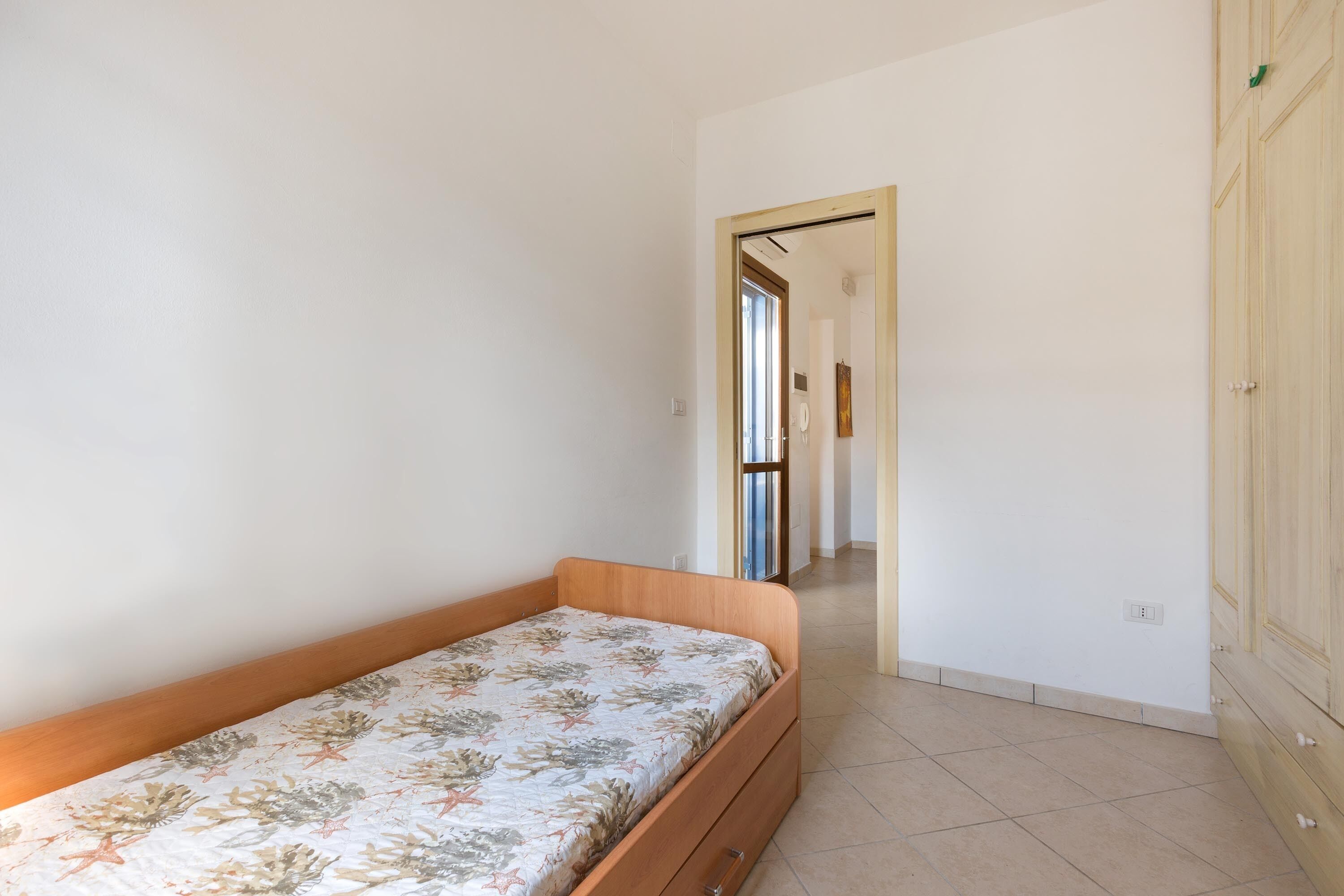 A bedroom with a single bed, a wardrobe, and a door leading to another room.