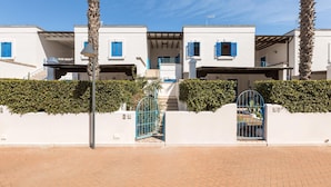 A row of white buildings with blue shutters, a paved entrance, and a gate.